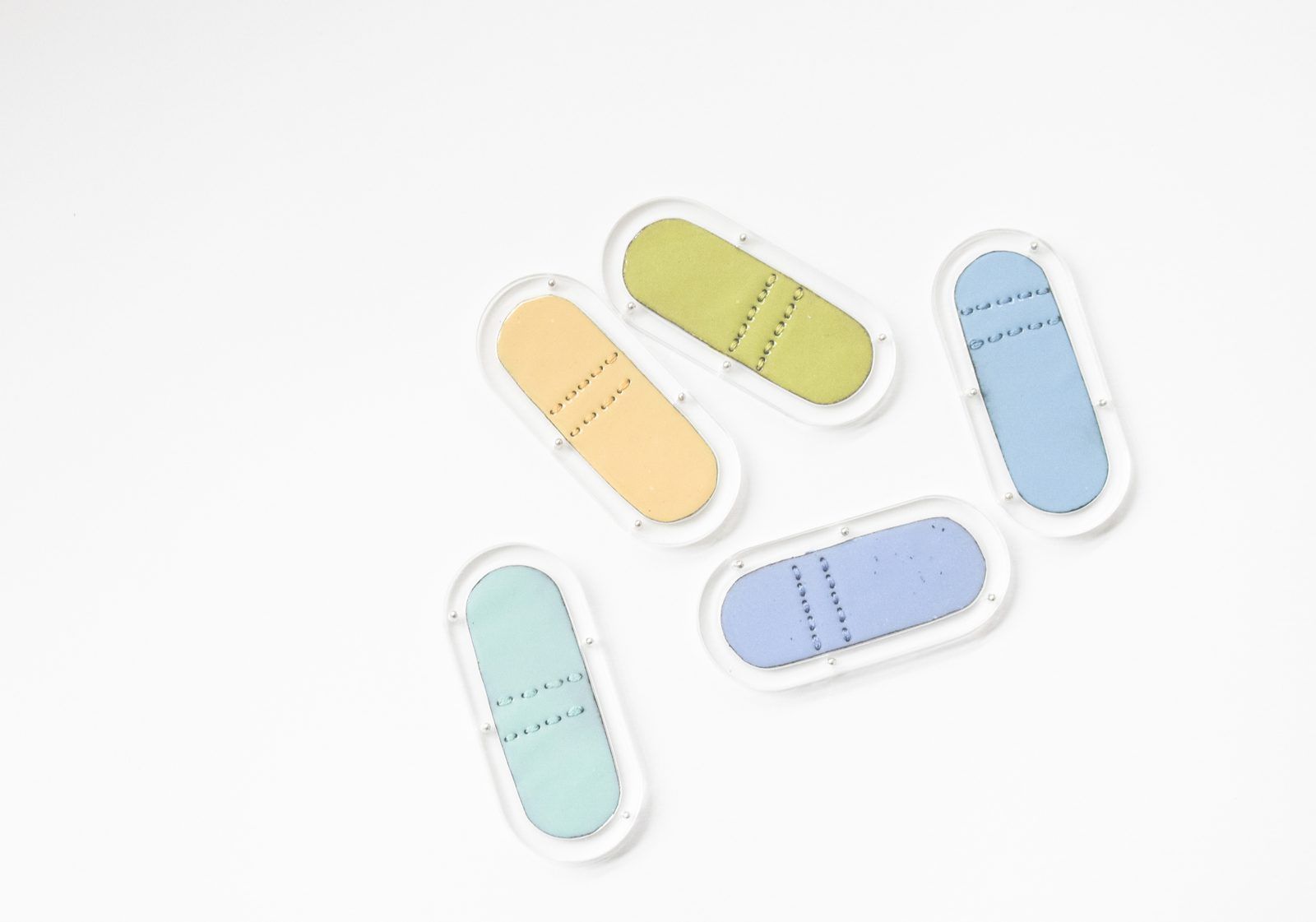 Pill-shaped enamel brooches in yellow, blue and mint